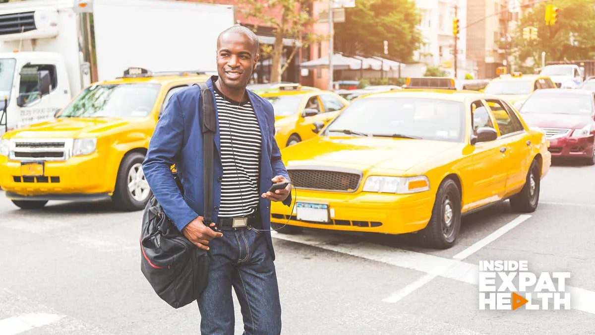 Young man walking across the road in the USA with yellow taxis behind him